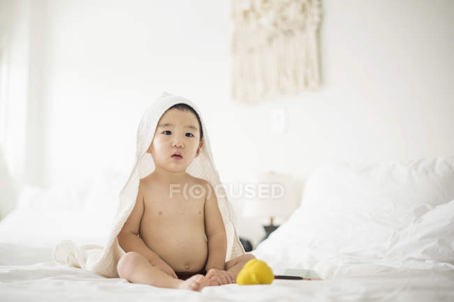 Niño pequeño con toalla blanca con capucha en la cama - foto de stock