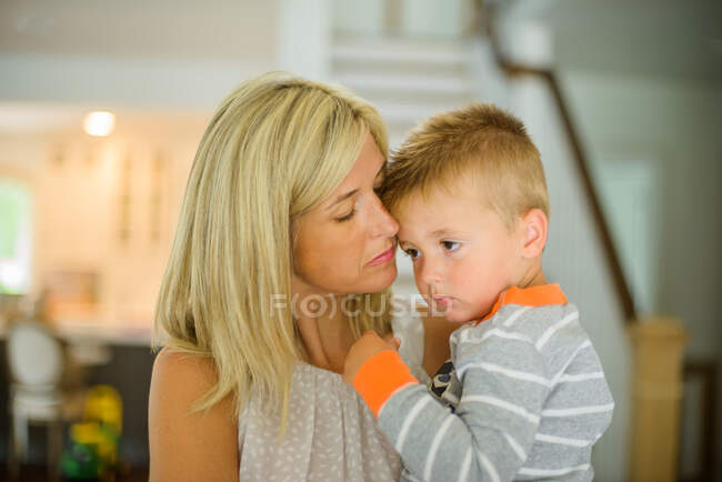 Femme adulte moyenne dans le salon avec tout-petit fils fatigué dans les bras — Photo de stock