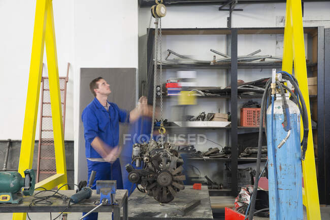 Male car mechanic hoisting car engine in repair garage — Stock Photo