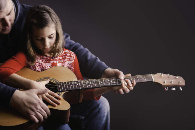 Padre enseñando a hija a tocar la guitarra - foto de stock