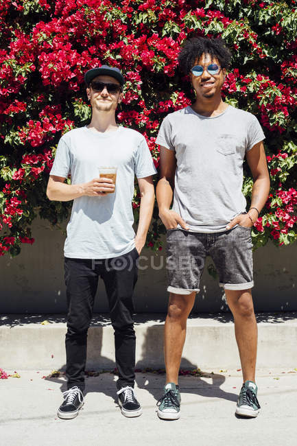Friends standing side by side with red bougainvilleas at background — Stock Photo