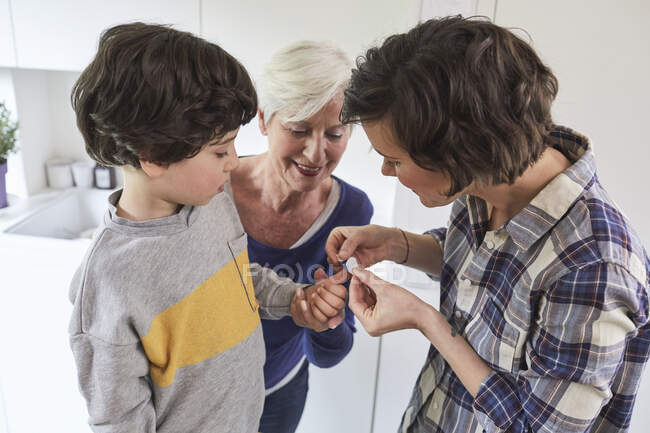 Mutter legt Gips auf den Finger des Sohnes, Großmutter hält die Hand des Enkels — Stockfoto