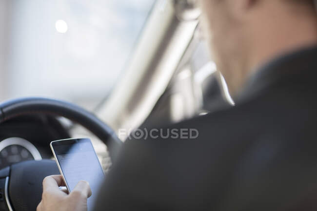 Geschäftsmann sitzt im Auto, schaut aufs Smartphone, Rückansicht — Stockfoto