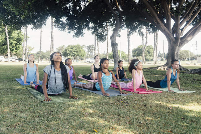 Las colegialas que practican yoga mirando hacia arriba posan en el campo deportivo de la escuela - foto de stock