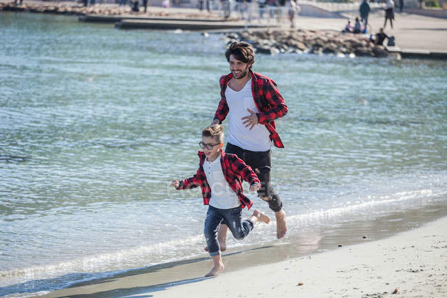 Padre e hijo corriendo a lo largo de la playa - foto de stock