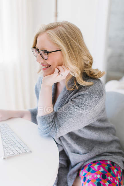 Mujer joven sentada en la mesa y mirando el ordenador - foto de stock