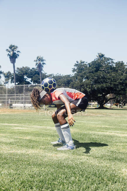 Écolière adolescente footballeuse équilibrant le ballon sur les épaules sur le terrain de sport scolaire — Photo de stock