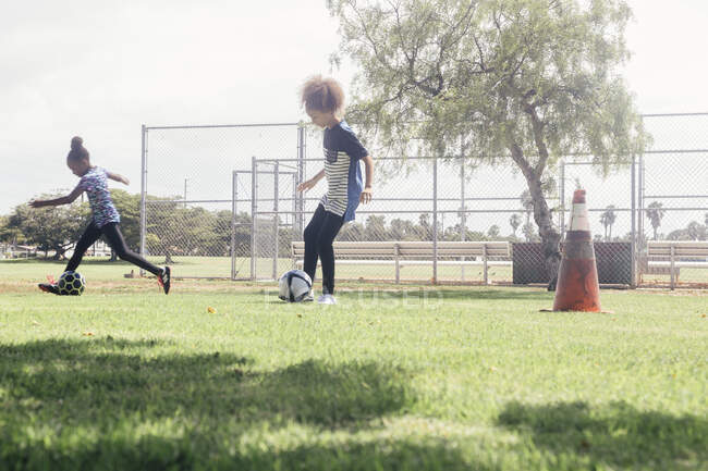 Colegialas haciendo driblar la práctica de pelota de fútbol en el campo de deportes de la escuela - foto de stock