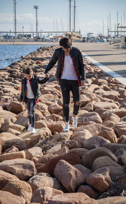 Pai e filho caminhando sobre rochas ao lado do mar — Fotografia de Stock