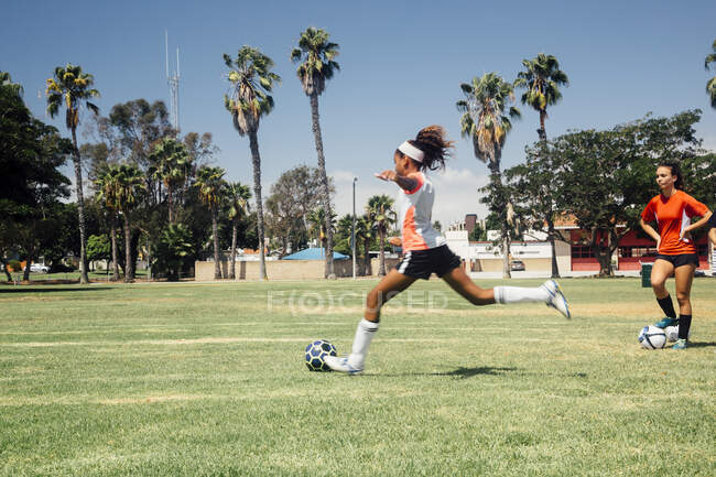 Écolière adolescente donnant un coup de pied au ballon de soccer sur le terrain de sport scolaire — Photo de stock
