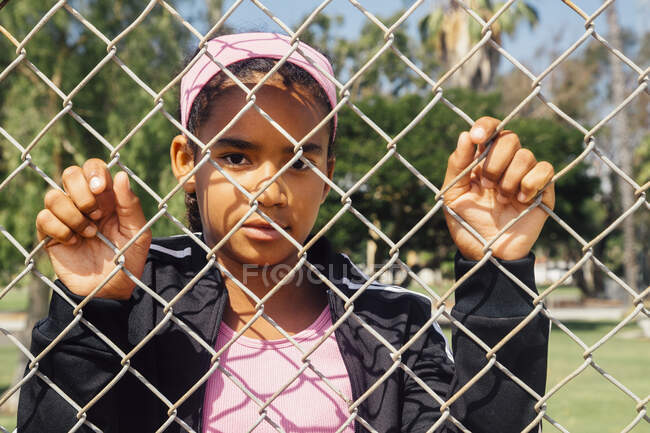 Portrait of schoolgirl holding wire fence on school sports field — Stock Photo