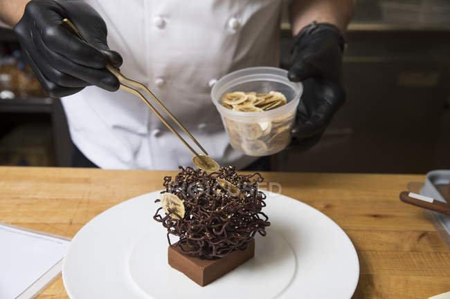 Chef posizionare fette di banana secca sulla decorazione torta nido di cioccolato — Foto stock