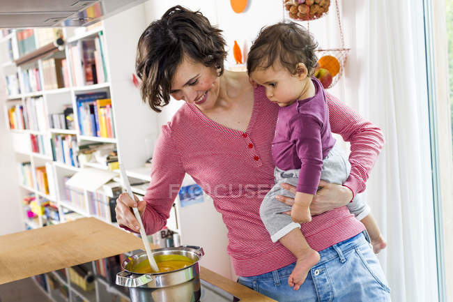 Мати тримає дівчинку під час приготування їжі на кухні — стокове фото