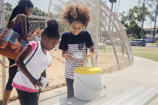 Schoolgirls preparing drinks from cool box on school sports field — Stock Photo