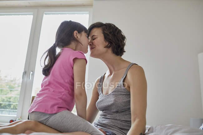 Mãe e filha em casa, sentadas juntas, tocando narizes — Fotografia de Stock