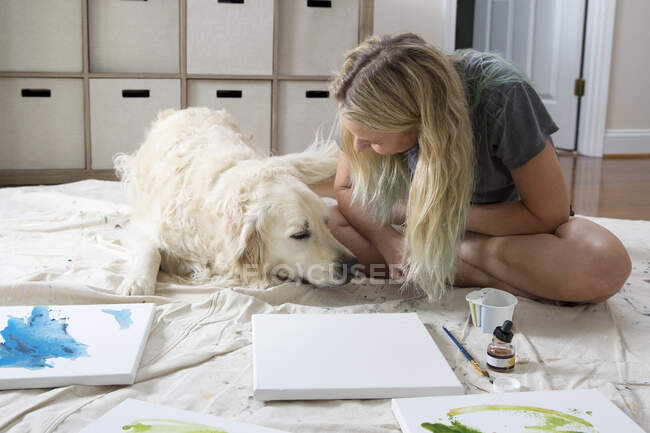 Female artist sitting on dust sheet petting dog in studio — Stock Photo