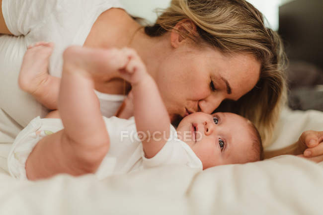 Donna baciare figlia bambino sul letto — Foto stock