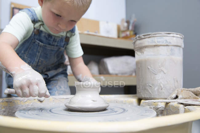 Boy cutting pot from potter wheel — Stock Photo