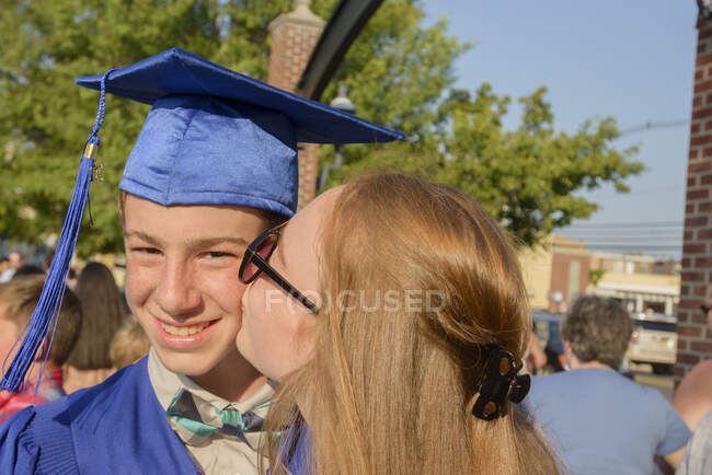 Девушка целует мальчика в щеку на церемонии вручения дипломов — стоковое фото