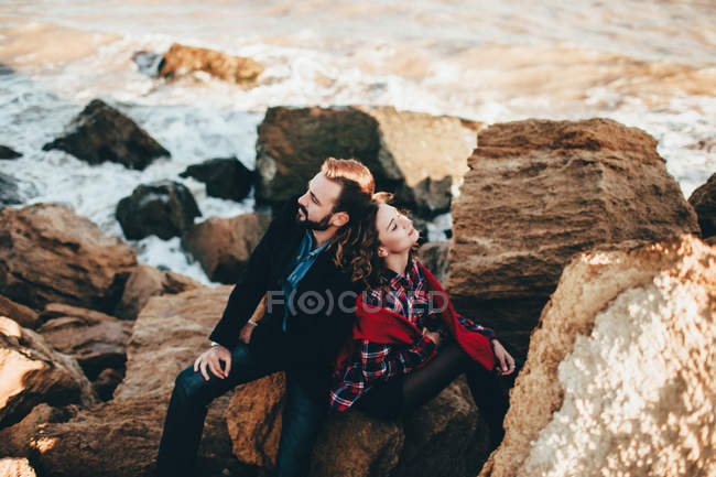 Romántica pareja adulta sentada espalda con espalda en la roca de playa, Óblast de Odessa, Ucrania - foto de stock