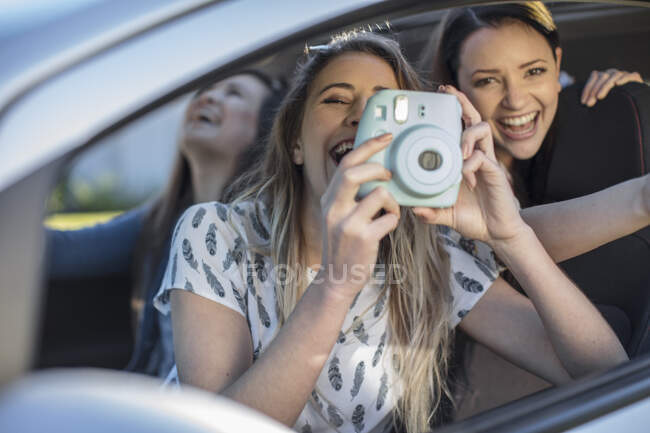 Молода жінка в машині з двома друзями, роблячи фотографії з вікна машини — стокове фото