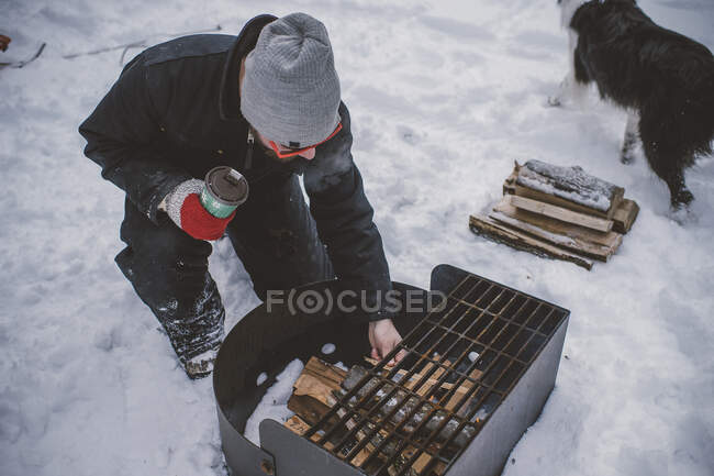Young man preparing to light barbecue fire in snow — Stock Photo