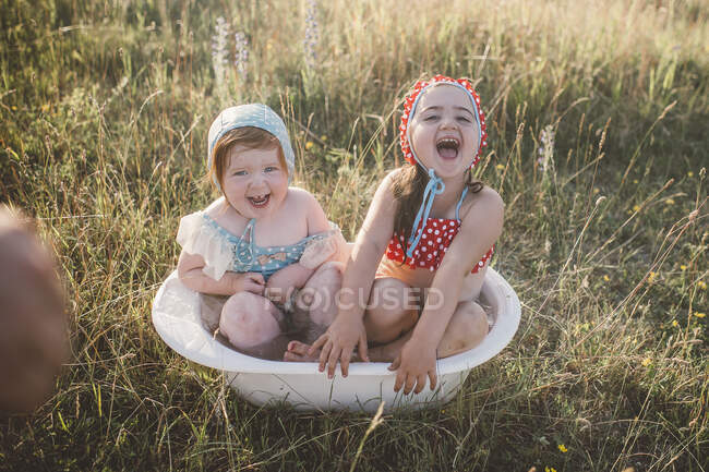 Two girls in field, playing in plastic tub of water — Stock Photo