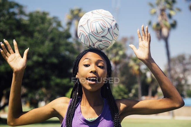 Adolescente colegiala jugador de fútbol balanceo pelota en la cabeza en el campo de deportes de la escuela - foto de stock