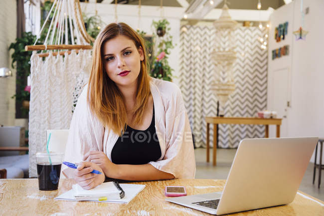 Кавказька жінка сидить за столом у творчій студії і дивиться на камеру, посміхаючись — стокове фото
