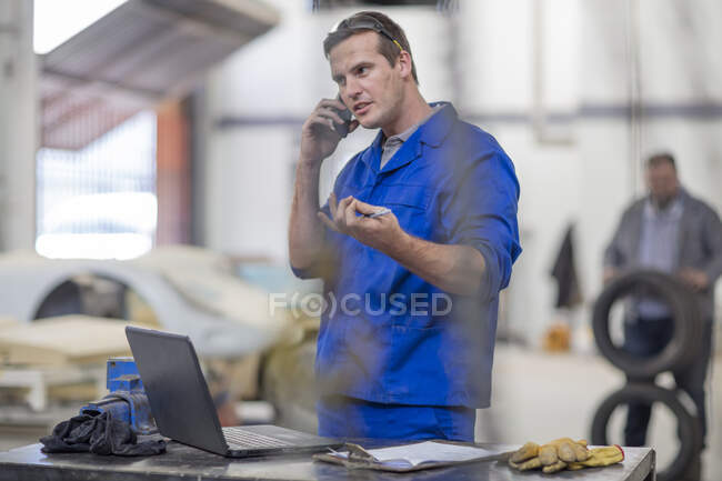 Автомеханик делает звонок на смартфон в ремонтном гараже — стоковое фото