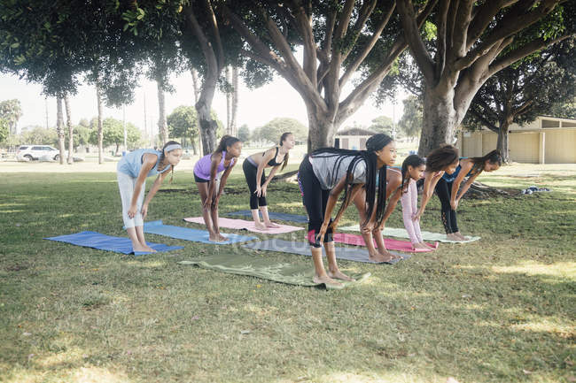 Colegialas practicando yoga posan en el campo deportivo de la escuela - foto de stock