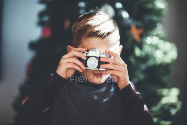 Portrait of boy taking photo and Christmas tree at background — Stock Photo