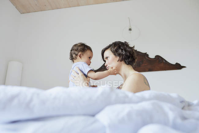 Mãe sentada na cama com bebê menina — Fotografia de Stock