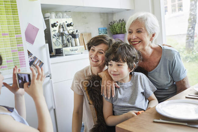 Молодая девушка фотографирует, брат, мать и бабушка, используя смартфон — стоковое фото
