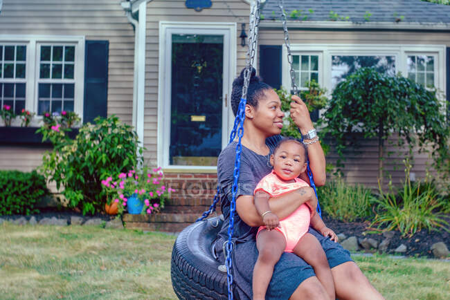 Mid adult woman on garden tire swing with baby daughter — Stock Photo