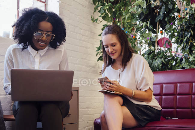 Colleagues sitting together on sofa in office using laptop — Stock Photo