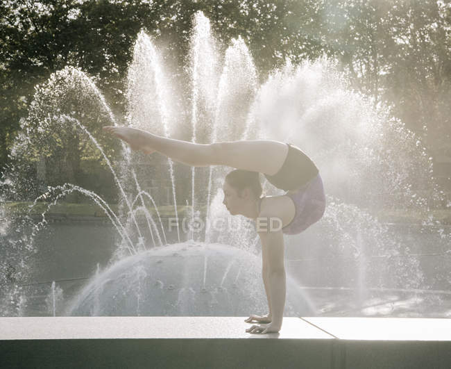 Teenage girl beside fountain balancing on hands — Stock Photo