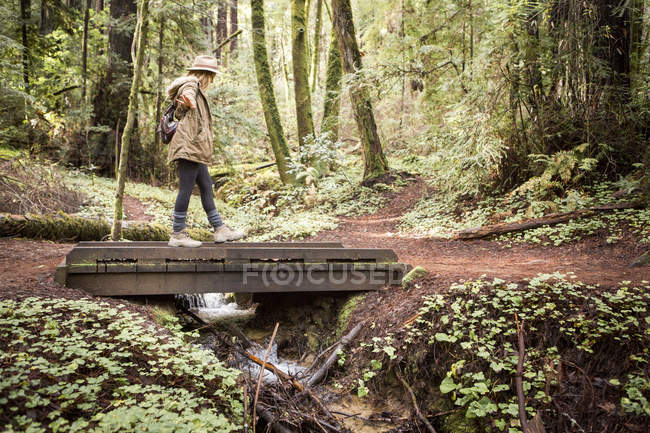 Giovane donna nella foresta in equilibrio sul ponte pedonale — Foto stock