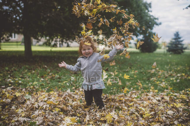Retrato de vermelho peludo fêmea criança no parque jogando folhas de outono — Fotografia de Stock
