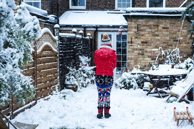 Vista trasera de la mujer de pie en el jardín cubierto de nieve - foto de stock