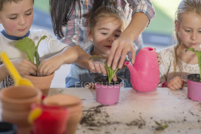 Mujer adulta que ayuda a los niños pequeños con la actividad de jardinería - foto de stock