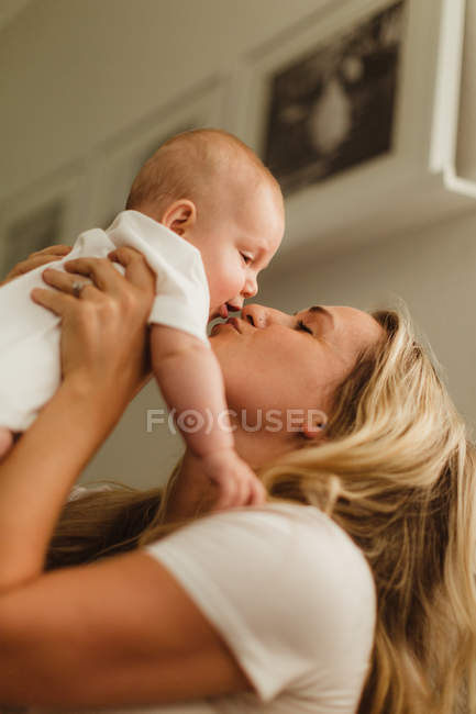 Woman holding up and kissing baby daughter — Stock Photo