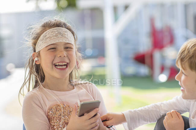 Молода дівчина тримає смартфон, у навушниках, сміється — стокове фото