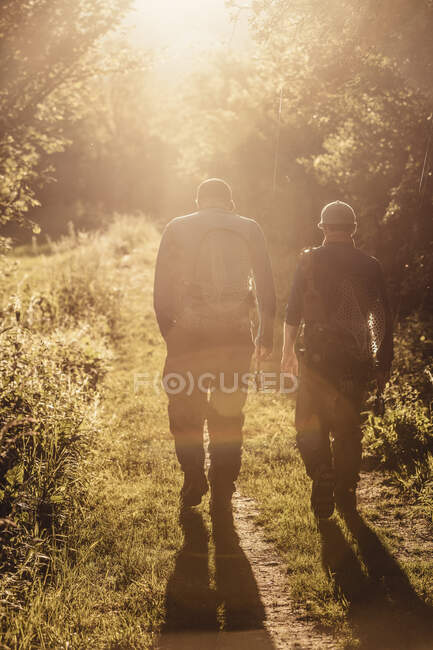 Veduta posteriore di due pescatori che passeggiano nel bosco al tramonto, Mozirje, Brezovica, Slovenia — Foto stock