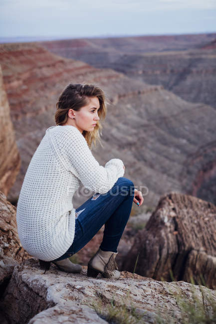 Mujer joven sentada en las rocas y mirando a la vista, Mexican Hat, Utah, EE.UU. - foto de stock