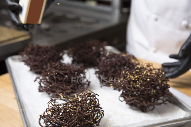 Chef spruzzando decorazioni dorate su nidi di cioccolato — Foto stock
