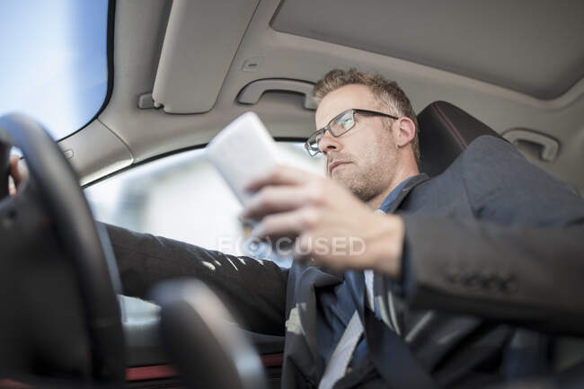 Businessman driving car, holding smartphone, low angle view — Stock Photo