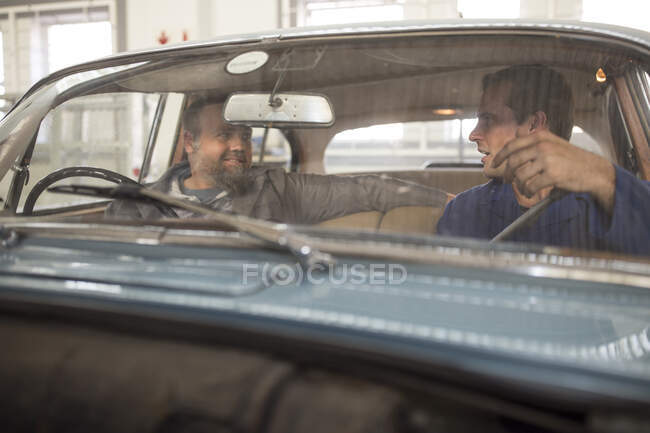 Zwei Automechaniker unterhalten sich auf dem Beifahrersitz eines Oldtimers in der Werkstatt — Stockfoto