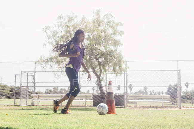 Adolescente colegiala haciendo driblar pelota de fútbol práctica en el campo de deportes de la escuela - foto de stock