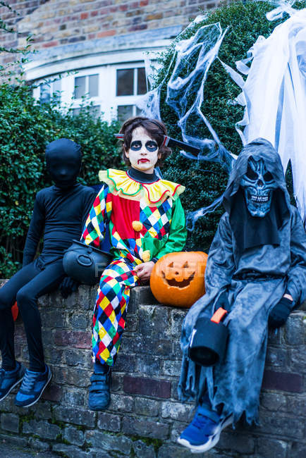 Ritratto di tre ragazzi in costume di Halloween, seduti sul muro — Foto stock